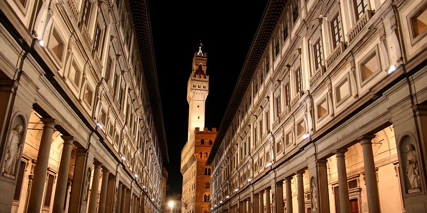An image of Florence's Uffizi Gallery at night, showcasing symmetrical Renaissance columns, facades, and illuminated Palazzo Vecchio.