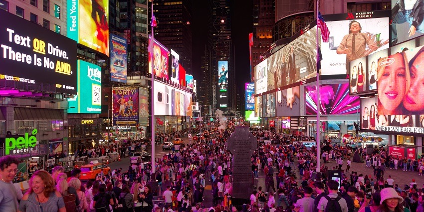 An image of Times Square, a famous place to visit in New York, features bright lights and billboards.