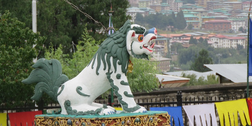 An image of the chorten surrounded by dense greenery and stunning mountains.