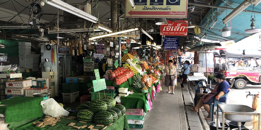 A picture of Maeklong Railway Market with tourists and vendors interacting.