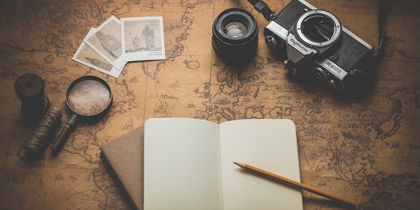 A notebook with a pencil is lying on a vintage map alongside a camera and travel items.