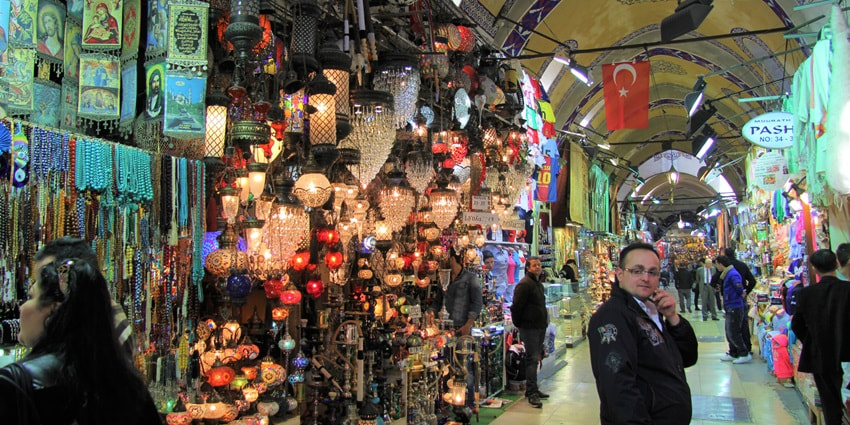 A colourful shot of the Turkish Grand Bazaar with tourists venturing into stores with vibrant textiles, spices, and souvenirs.