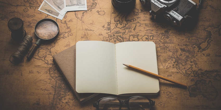 A notebook with a pencil is lying on a vintage map alongside a camera and travel items.