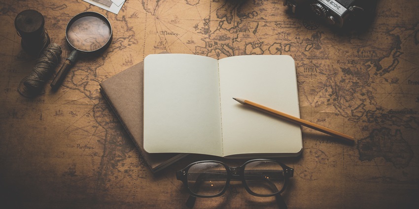 A notebook with a pencil is lying on a vintage map alongside a camera and travel items.