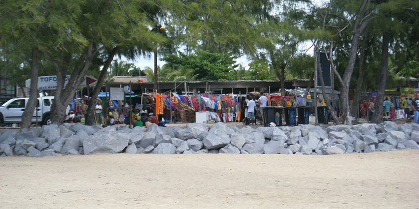 Tofo market with multiple shops, vendors, clothes hanging in the shops and people standing