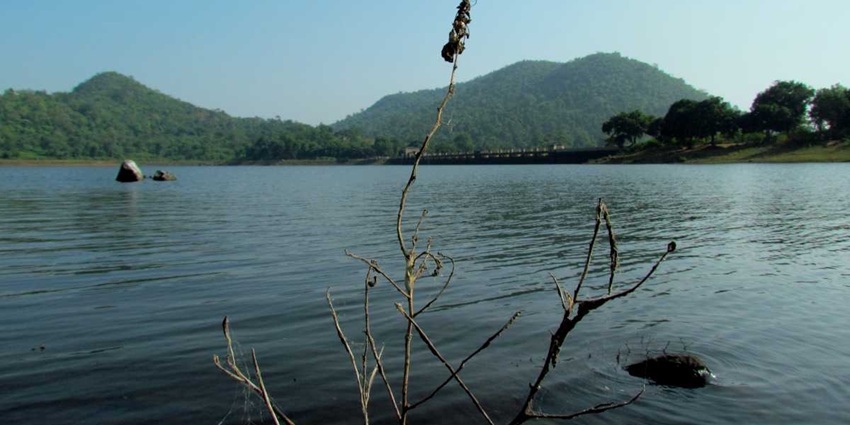 Topchanchi Lake with calm waters, greenery all around, and hills and shoreline views.