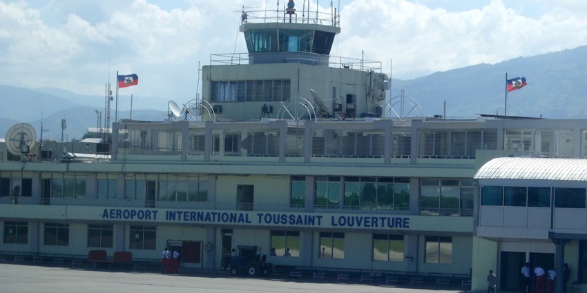 Aéroport International Toussaint Louverture building with control tower and Haitian flags.