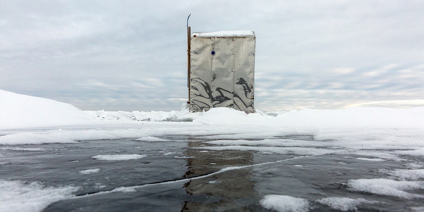 Tin Ice fishing house on the frozen body of the lake surrounded by the white snow