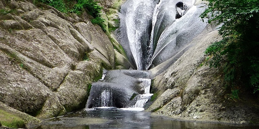 A scenic view of Todo Waterfall cascading down rocky cliffs, surrounded by lush greenery.