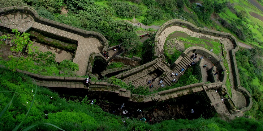 Structure of Lohagad fort from above, surrounded by greenery, with people exploring the ruins