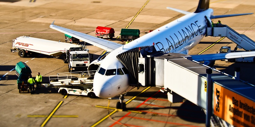 Ground crew members are loading luggage onto an aircraft connected to a jet bridge.
