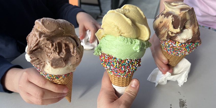 A picture of 3 ice cream cones served on a table at an ice cream parlour