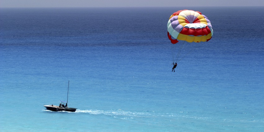 Image of a person parasailing high above the ocean, with bright canopy and trailing ropes