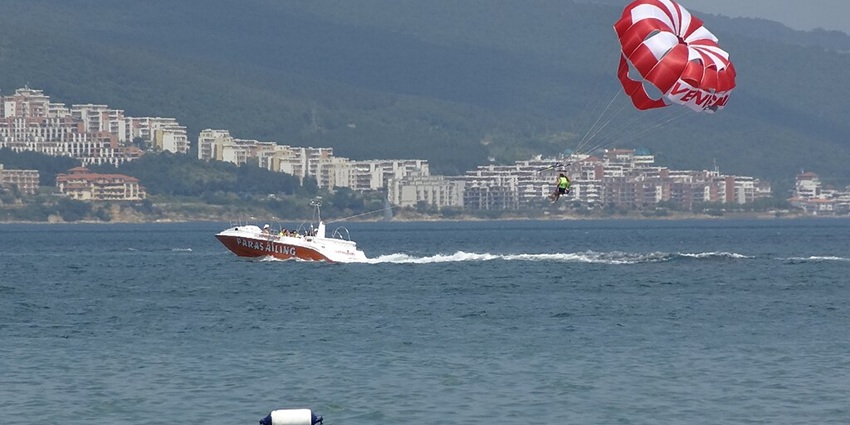 A person enjoys parasailing on a sunny day with a speed boat pulling it with a string.