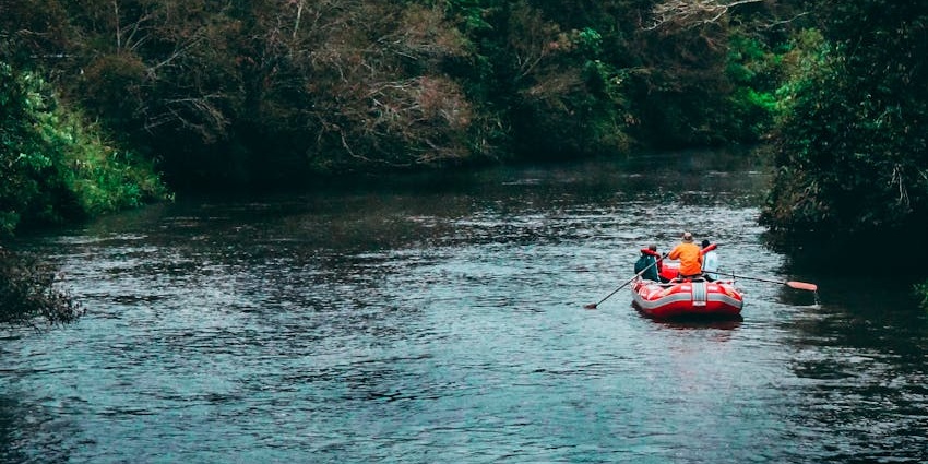 An image of a red inflatable raft with two people paddling, similar to the river rafting experience.