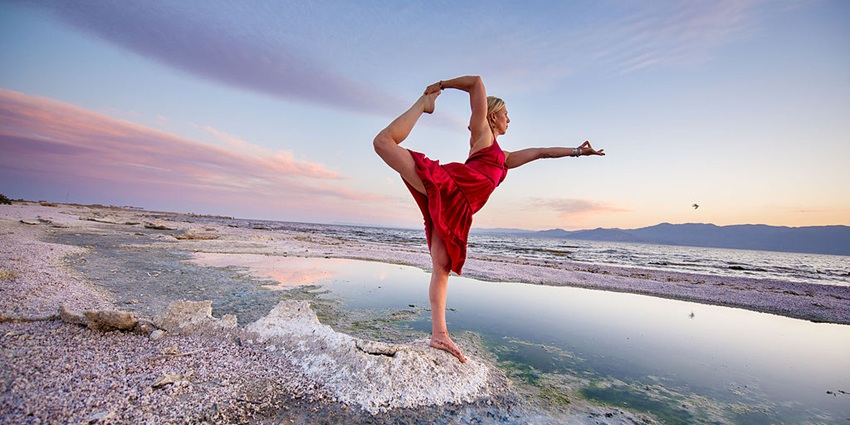 An image of a woman performing Natrajasana spectacularly at a beach near the sea.