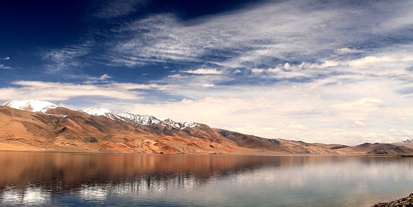 Tso Moriri lake with a still and large water body, sandy shoreline and snowy mountain peaks