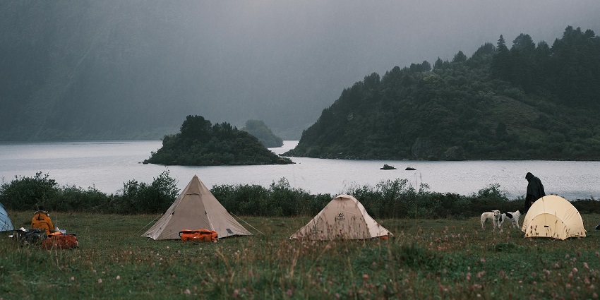 Wide angle view of the tents by the lake and foggy mountains far beyond