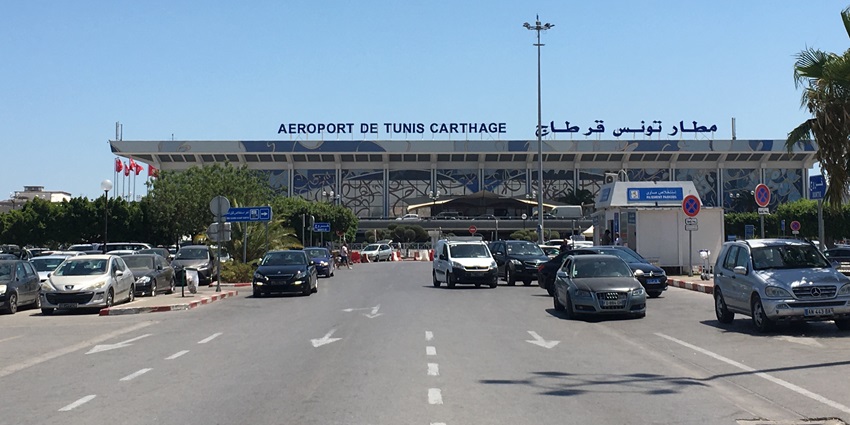 Facade of Tunis-Carthage International Airport with the nameplate on top and a busy road