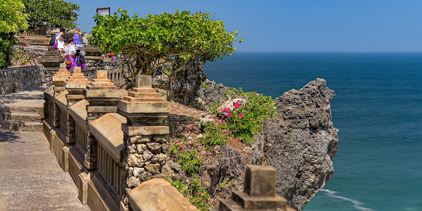 An image of a scenic view of Uluwatu Temple perched on a cliff with waves crashing below