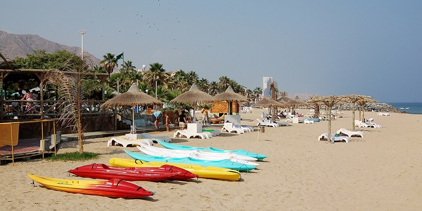 A picture of a beach with numerous shacks and umbrellas, with kayaks placed around the edge