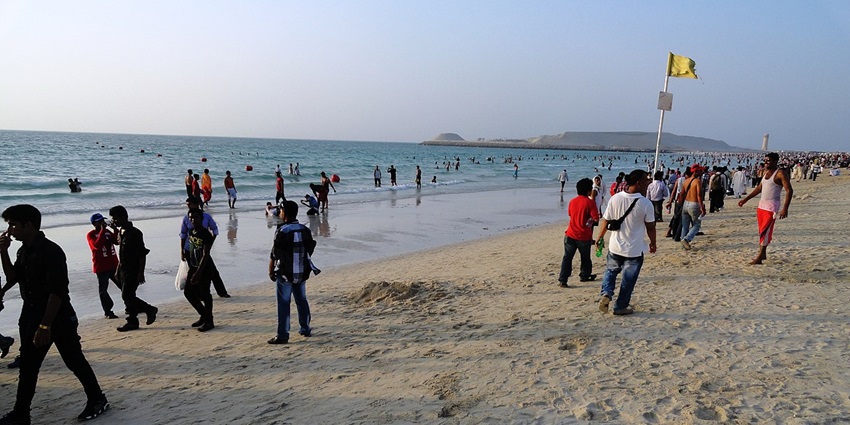 A lively day at the beach, with people walking, swimming, and relaxing by the shoreline.