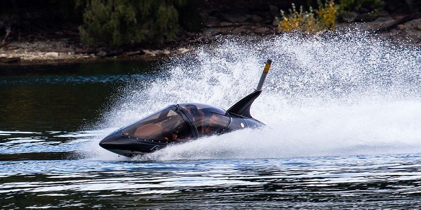 A black shark-inspired jet boat speeds across the water, creating a dramatic splash