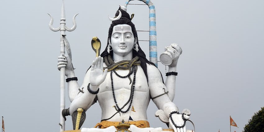 A large, white statue of Shiva with four arms, holding a trident and other objects
