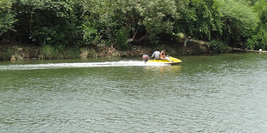 Lake with a couple of people riding a yellow motorboat while wearing a safety jacket