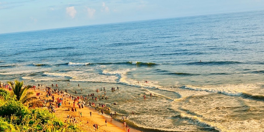 An image of Varkala Beach with red cliffs, golden sand, and blue waters under a clear sky.