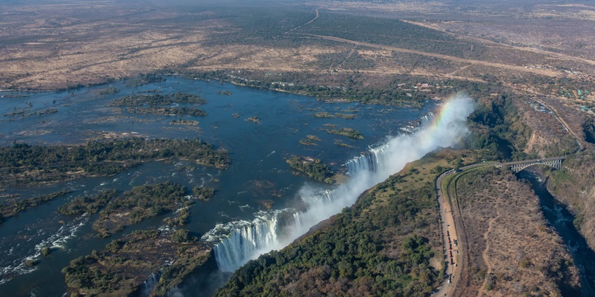 An aerial view of a majestic waterfall in the middle of a lush green forest in Zambia