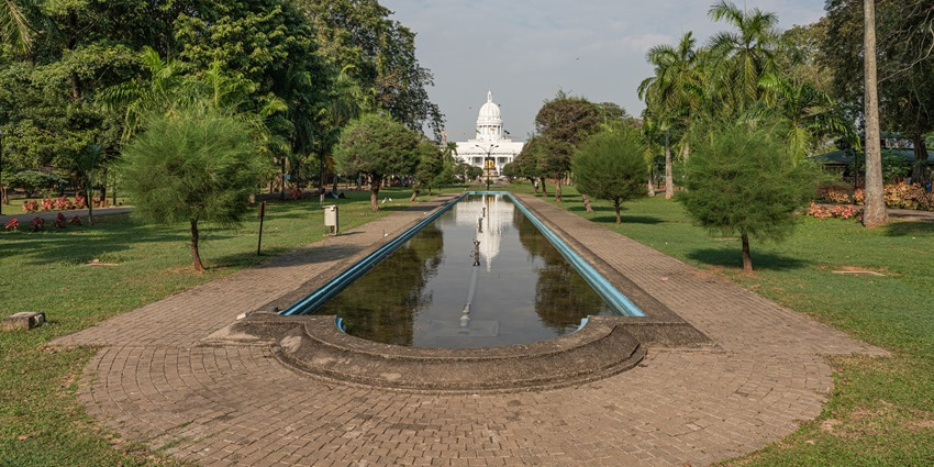 An image of the Viharamahadevi Park with a reflecting pool, lush greenery, and a domed white building