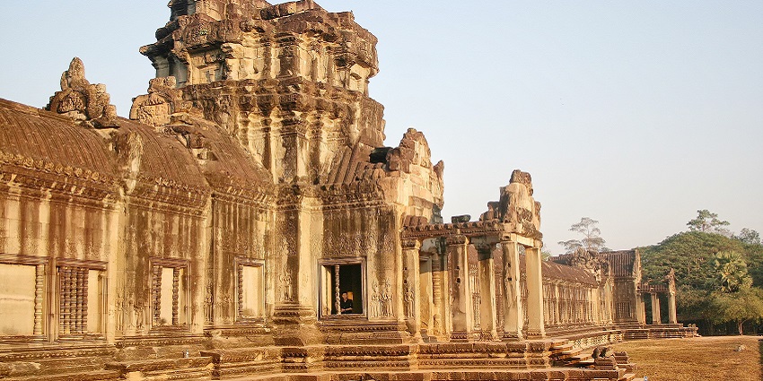 An image of the ancient stone temple of Angkor Wat, with intricate carvings, partially ruined, under a bright blue sky.