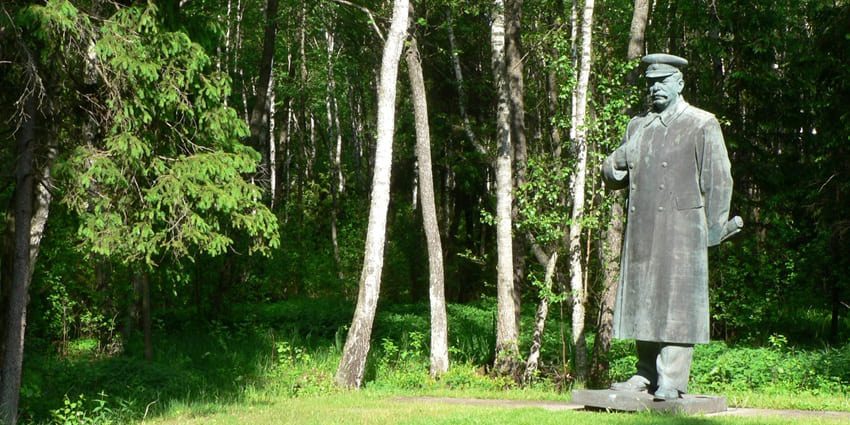 A tall statue of Stalin placed on the green grass in Grutas Park, surrounded by trees and greenery.