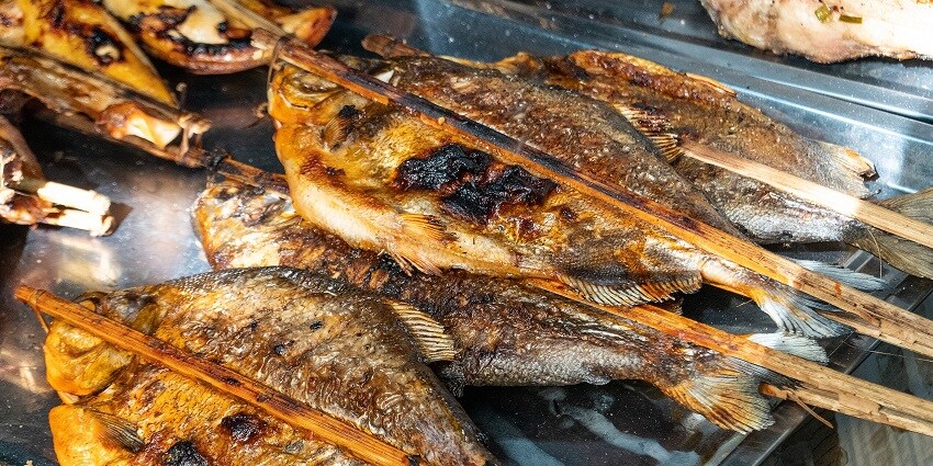 Grilled fish with charred skins, laid closely together on a tray in the Crab Market