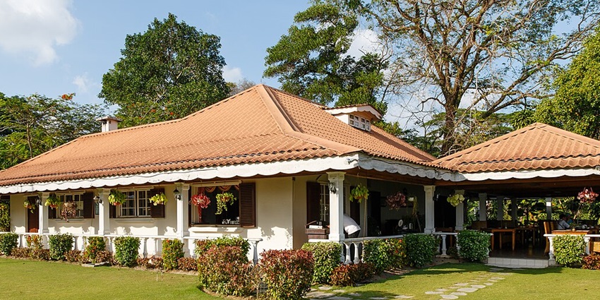 An image of a single-story Sabah Tea Garden with a terracotta-tiled roof, wrap-around porch, and greenery around