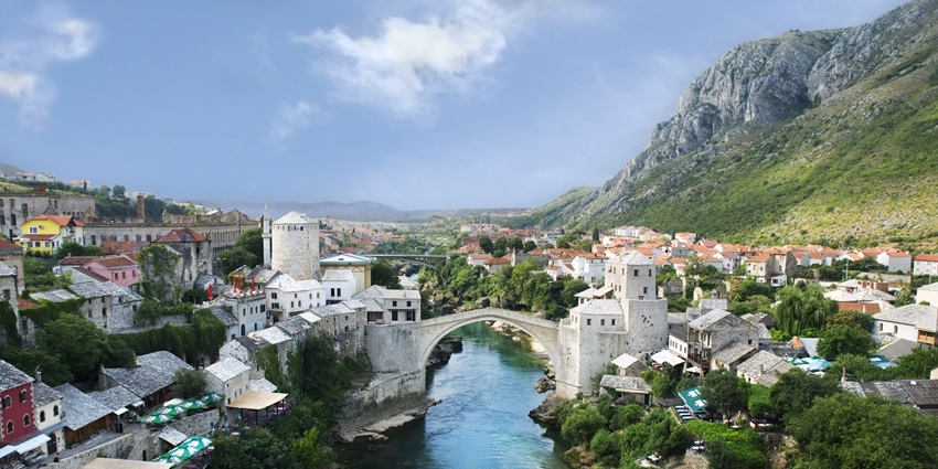 In a village, an old bridge arches over a waterbody as stone houses flank both sides.