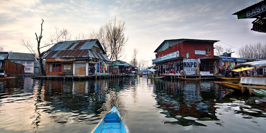 Floating market in Srinagar with multiple shops, a blue boat and dried trees alongside