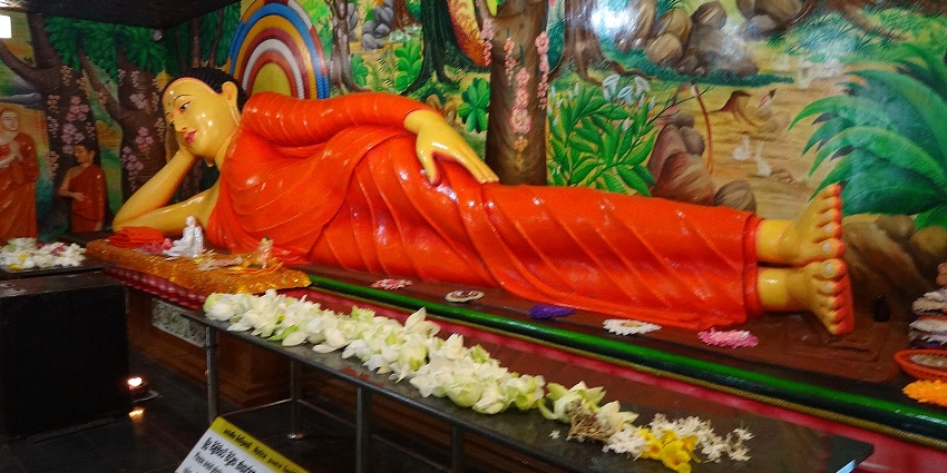 Reclining Buddha statue in Mihintale Temple, adorned with flowers and vibrant art