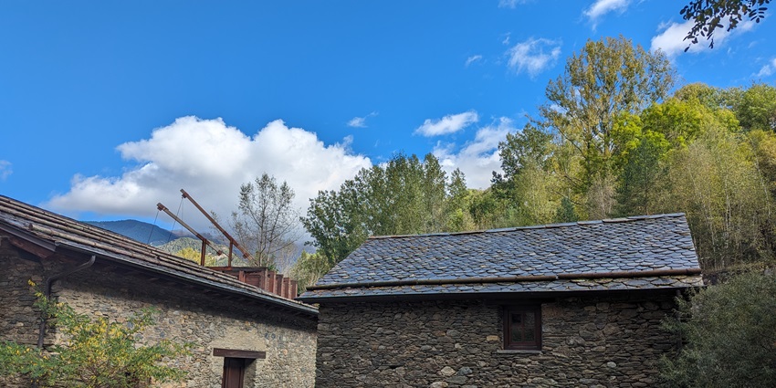 The town of Farge Rossell features two stone houses, trees, and mountains in the distance.