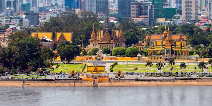 An image of the golden-roofed Phnom Penh Palace with intricate design, surrounded by green trees and visiting tourists.