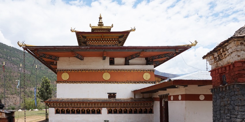 An image of three Buddhist nuns in red robes standing on a path, prayer flags fluttering nearby
