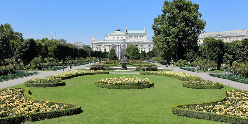 Volksgarten in Vienna with blooming flower beds, classical statues, and historic architectural backdrop.