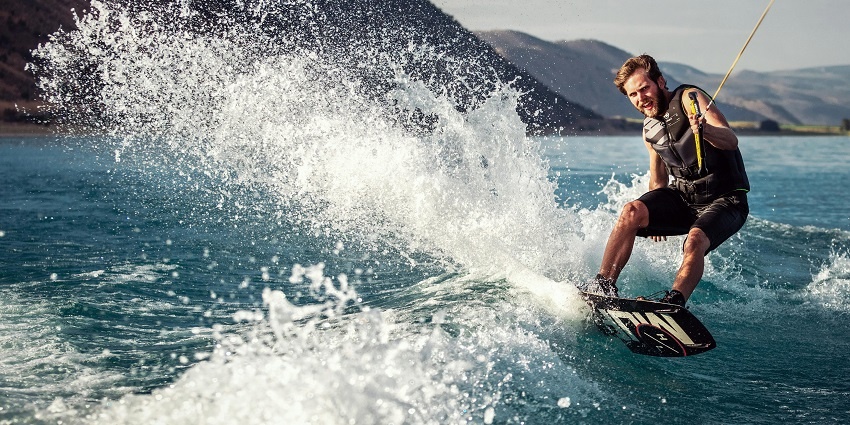 An image of a woman wakeboarding with a red life jacket and helmet, surrounded by water.