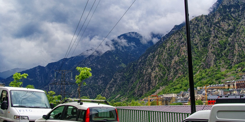 The roads of Andorra La Vella with a few cars parked, blue mountains, and clouds hovering above.