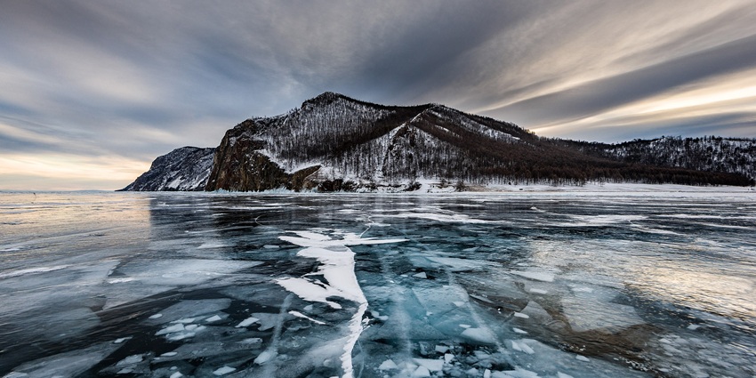 Baikal Lake with a thick frozen body and trees on the snow-covered mountains afar.