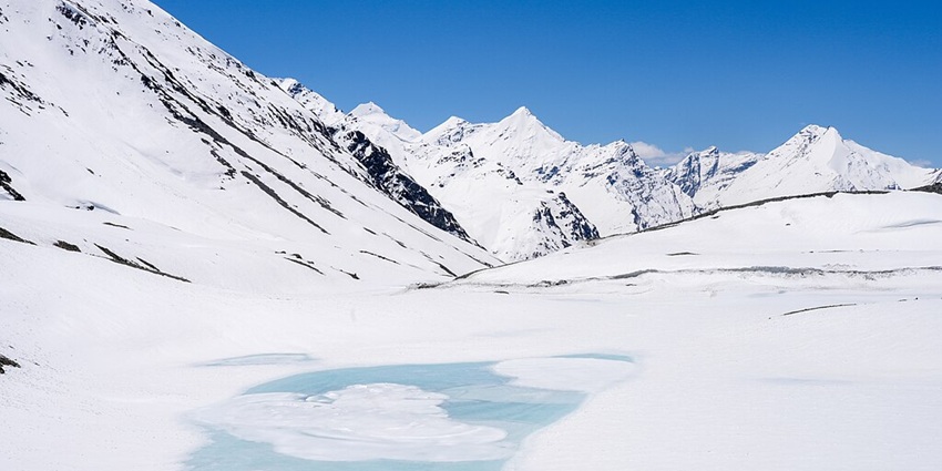 Frozen lake with thick ice, surrounded by white snow and snowy mountains under a blue sky