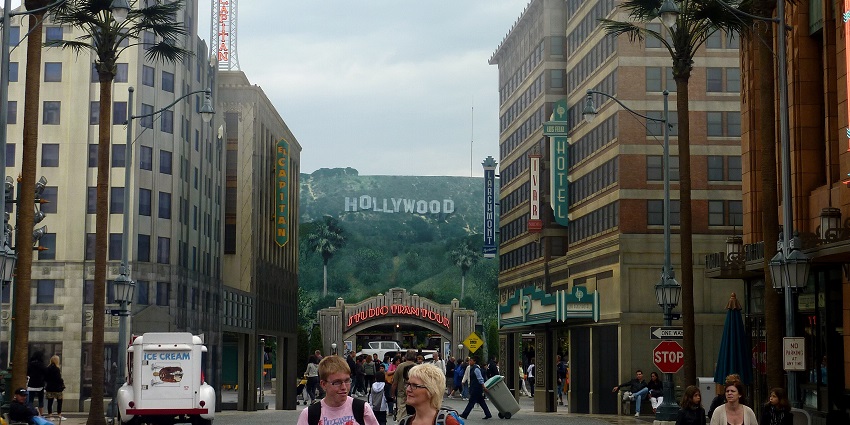 Walk down a street lined with palm trees and tall buildings, facing the Hollywood sign