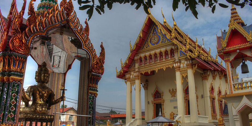 An image of the Wat Chetawan Temple adorned with intricate details, a foreground statue, and traditional architecture