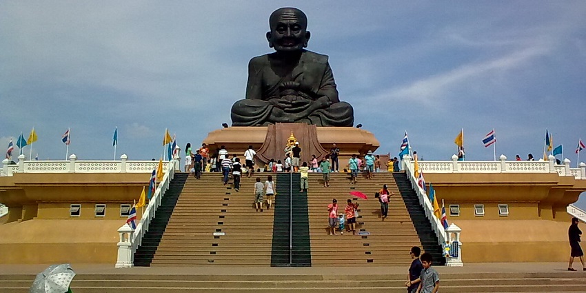 The giant statue of Luang Phor Thuad at Wat Huay Mongkol temple is surrounded by greenery.